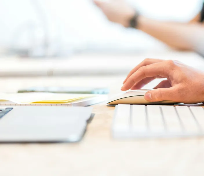 A hand hovers over a mouse with a white keyboard and laptop in front